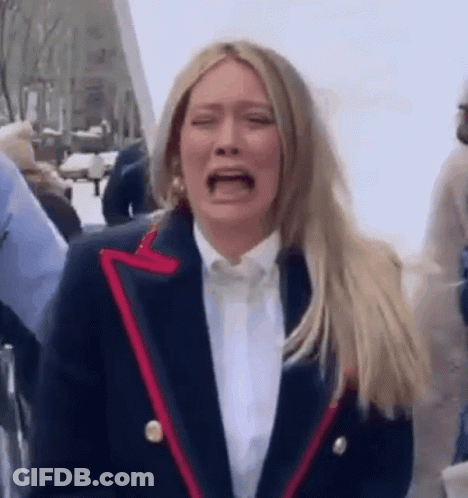 A Woman In A Suit Is Crying While Standing In A Crowd Of People . GIF