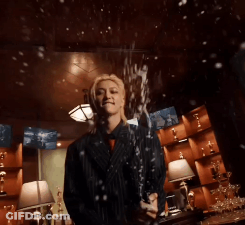 A Woman In A Suit Is Holding A Bottle Of Champagne In A Room . GIF