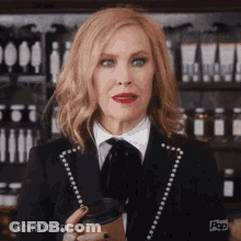 A Woman In A Suit Is Holding A Cup Of Coffee In Her Hand . GIF