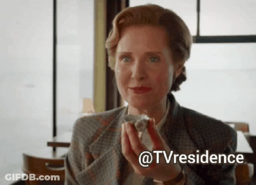 A Woman In A Suit Is Holding A Piece Of Cake In Her Hands . GIF