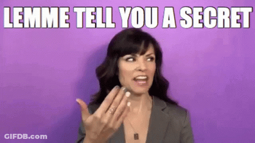A Woman In A Suit Is Making A Funny Face And Says Lemme Tell You A Secret . GIF