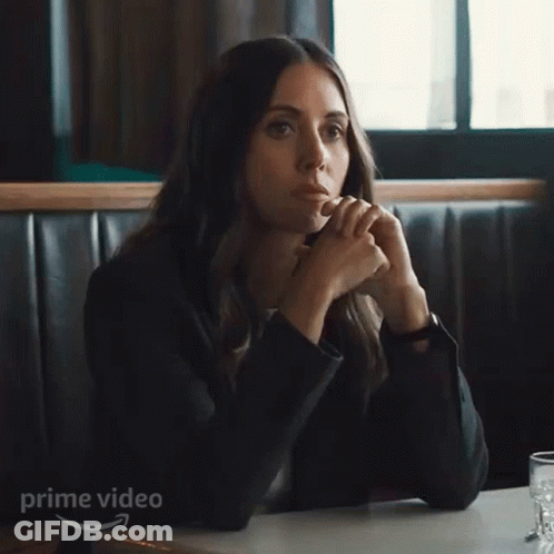A Woman In A Suit Is Sitting At A Table With Her Hands Up In Front Of A Sign That Says Prime Video . GIF
