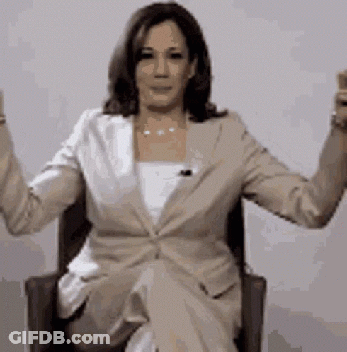 A Woman In A Suit Is Sitting In A Chair With Her Arms Up . GIF