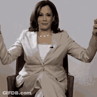 A Woman In A Suit Is Sitting In A Chair With Her Arms Up . GIF