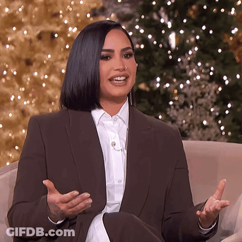 A Woman In A Suit Is Sitting In Front Of A Christmas Tree . GIF