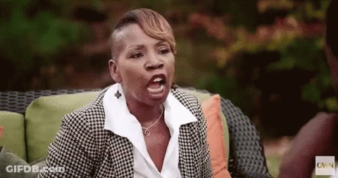 A Woman In A Suit Is Sitting On A Couch Making A Funny Face . GIF