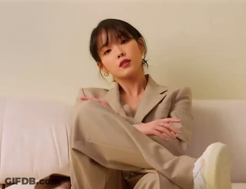 A Woman In A Suit Is Sitting On A Couch With Her Leg Up GIF
