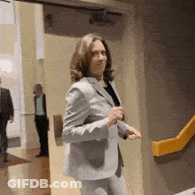 A Woman In A Suit Is Standing In A Hallway . GIF