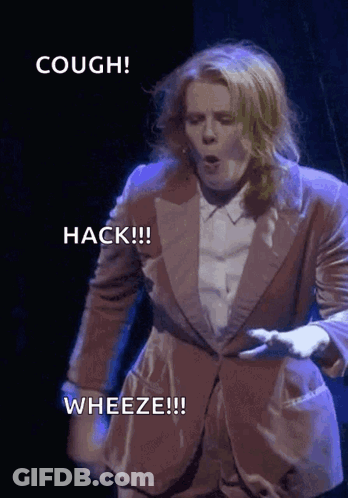A Woman In A Suit Says Hack Wheeze And Cough On A Stage GIF