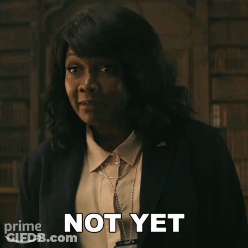 A Woman In A Suit Says " Not Yet " In Front Of A Bookshelf GIF
