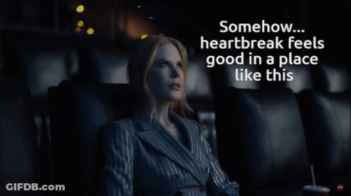 A Woman In A Suit Sits In A Dark Room With The Words " Somehow Heartbreak Feels Good In A Place Like This " Above Her GIF