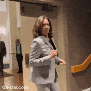 A Woman In A Suit Stands In A Hallway GIF