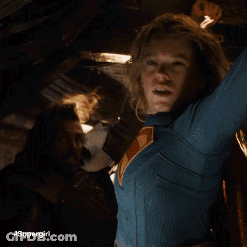 A Woman In A Supergirl Costume Is Holding A Light In Her Hand . GIF