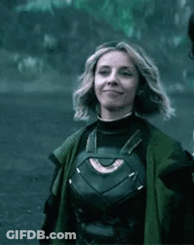 A Woman In A Superhero Costume Is Smiling And Wearing A Green Coat . GIF