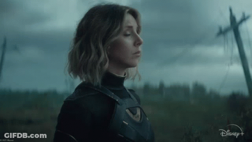 A Woman In A Superhero Costume Is Standing In A Field With A Telephone Pole In The Background . GIF