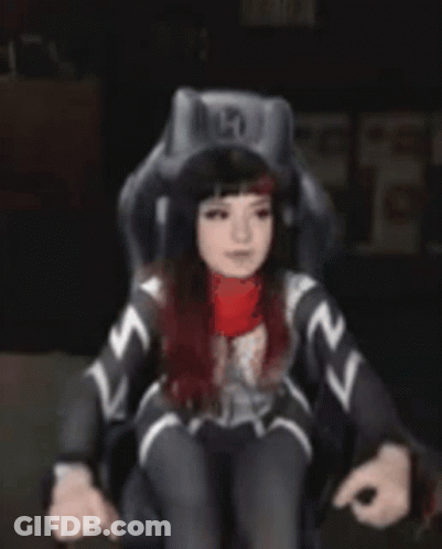 A Woman In A Superhero Costume Is Standing In Front Of A Chair . GIF