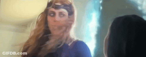 A Woman In A Superhero Costume Is Standing Next To Another Woman In A Room . GIF