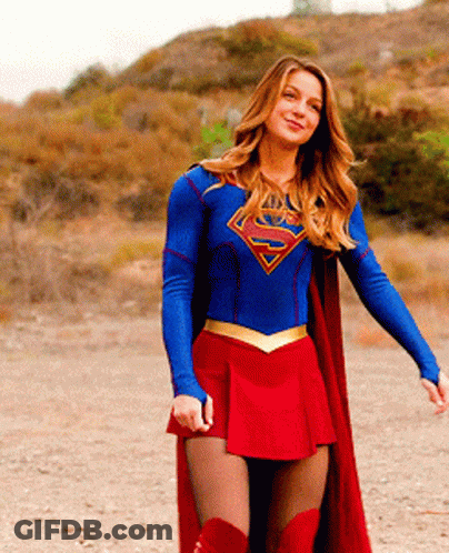 A Woman In A Superman Costume Is Standing In A Dirt Field GIF