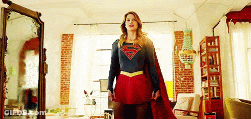 A Woman In A Superman Costume Is Standing In Front Of A Mirror . GIF