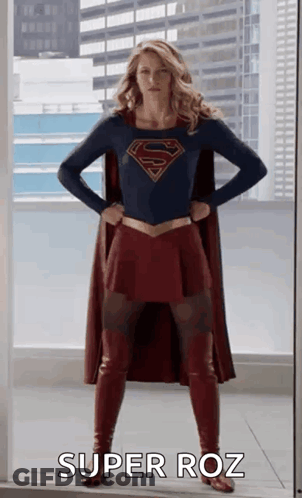A Woman In A Superman Costume Is Standing In Front Of A Window With Her Hands On Her Hips And Says Super Roz . GIF
