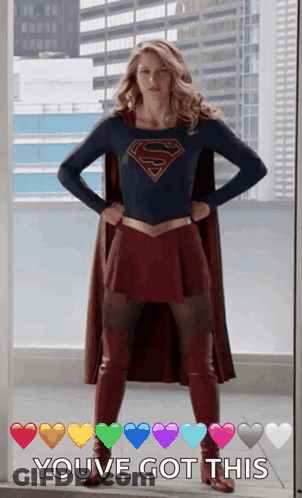 A Woman In A Superman Costume Is Standing In Front Of A Window With Her Hands On Her Hips .. GIF