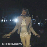 A Woman In A Tan Jacket Is Standing In The Dark GIF