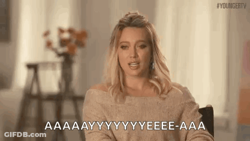 A Woman In A Tan Sweater Is Sitting In A Chair And Talking . GIF