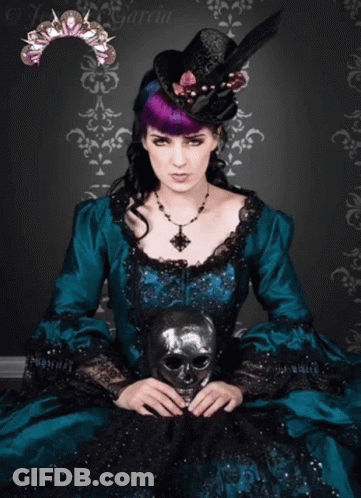 A Woman In A Teal Dress Holds A Skull Mask GIF