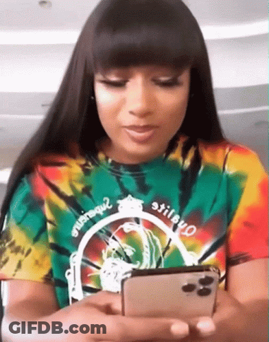 A Woman In A Tie Dye Shirt Is Looking At Her Cell Phone GIF