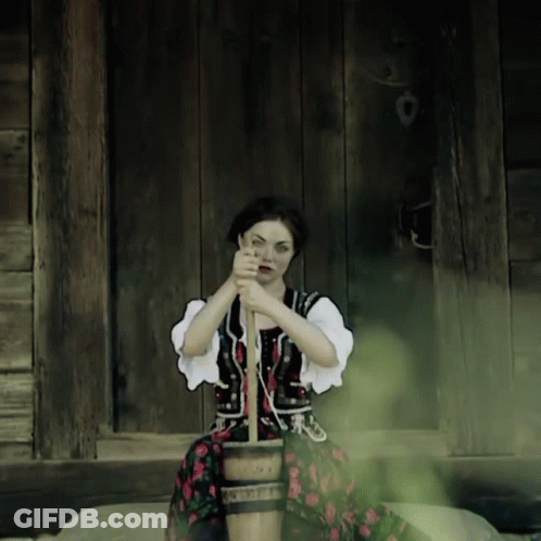 A Woman In A Traditional Costume Is Sitting On A Wooden Bucket GIF