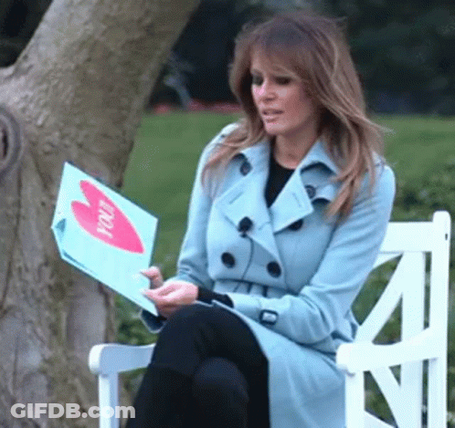 A Woman In A Trench Coat Is Sitting On A Bench Holding A Piece Of Paper That Says " You " GIF