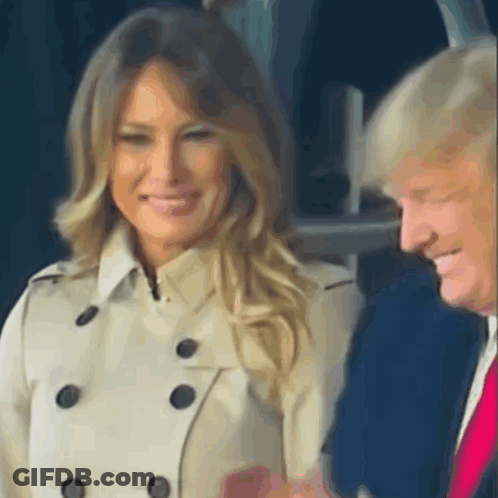 A Woman In A Trench Coat Is Smiling Next To A Man In A Suit . GIF