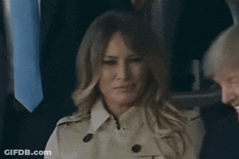 A Woman In A Trench Coat Is Smiling While Sitting Next To A Man In A Suit And Tie . GIF
