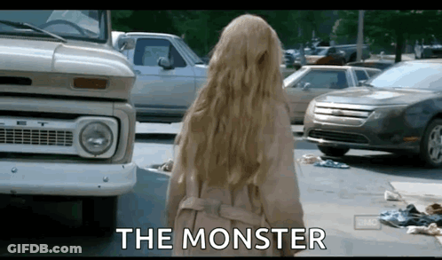 A Woman In A Trench Coat Is Standing In Front Of A Truck And Cars And The Words The Monster Are Written On The Screen . GIF