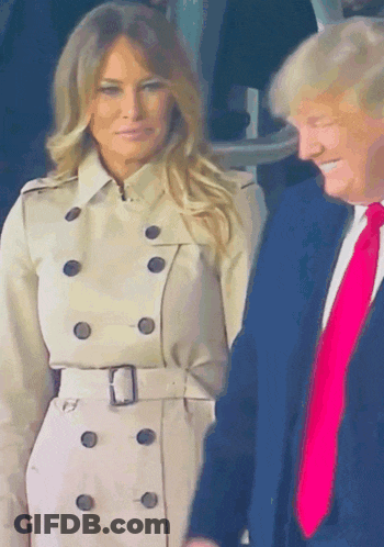 A Woman In A Trench Coat Stands Next To A Man In A Blue Suit GIF