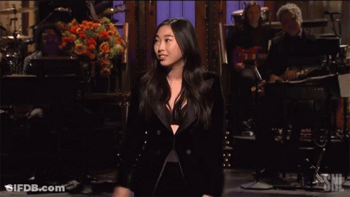 A Woman In A Tuxedo Is Singing On Stage In Front Of A Band GIF
