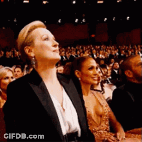 A Woman In A Tuxedo Is Sitting In Front Of A Crowd Of People . GIF