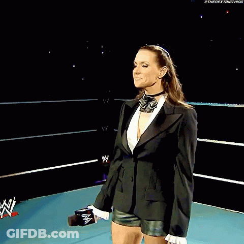 A Woman In A Tuxedo Stands In Front Of A Sign That Says Wrestlemania Principal Owner Of Stephanie Mcmahon GIF