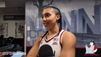 A Woman In A Uconn Basketball Uniform Is Talking Into A Microphone GIF