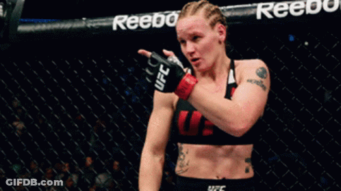 A Woman In A UFC Top Stands In A Cage GIF