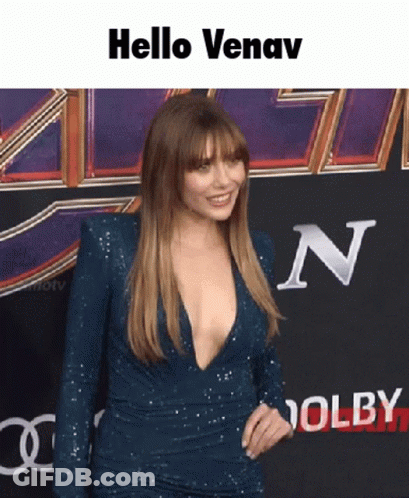 A Woman In A Very Plunging Blue Dress Is Standing On A Red Carpet And Says Hello Venav GIF
