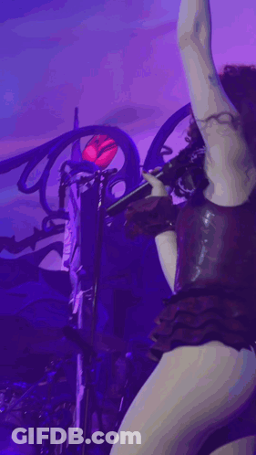 A Woman In A Very Revealing Outfit Is Singing Into A Microphone On Stage GIF