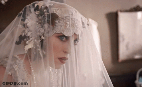 A Woman In A Wedding Dress Has A Veil Over Her Head GIF