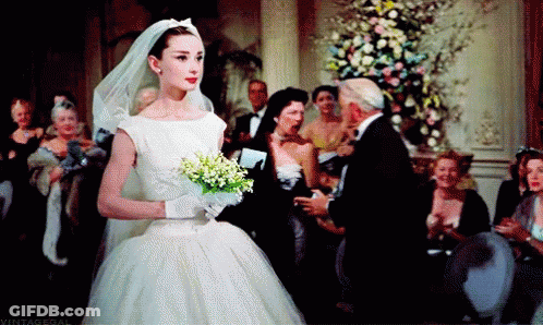 A Woman In A Wedding Dress Holds A Bouquet Of Flowers GIF