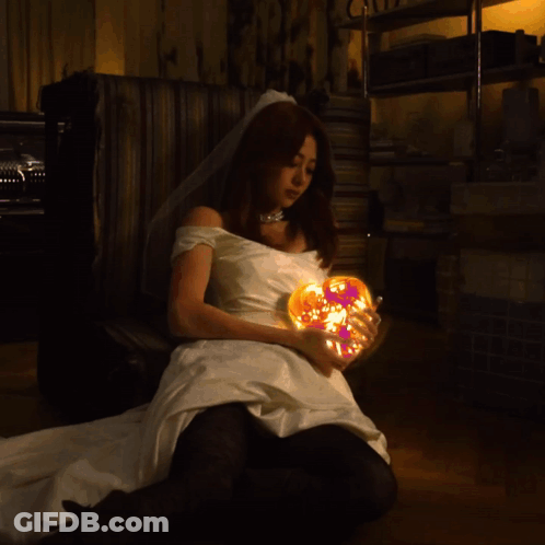 A Woman In A Wedding Dress Holds A Glowing Heart GIF