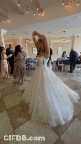 A Woman In A Wedding Dress Is Dancing With Her Arms In The Air GIF