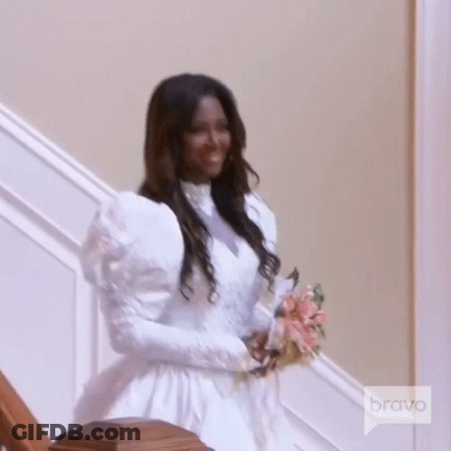 A Woman In A Wedding Dress Is Holding A Bouquet Of Flowers While Standing On A Set Of Stairs . GIF