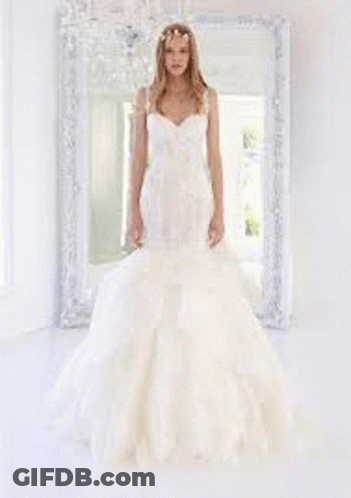 A Woman In A Wedding Dress Is Standing In Front Of A Window In A Room . GIF