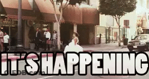A Woman In A Wedding Dress Is Walking Down A City Street With The Words `` It 'S Happening '' Written On It . GIF