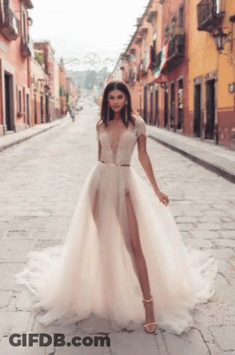 A Woman In A Wedding Dress Is Walking Down A Street . GIF